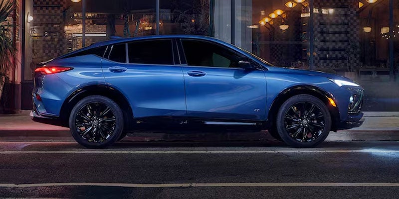 A blue Buick Envista SUV parked at night on a city street, with lights illuminated in a building behind it