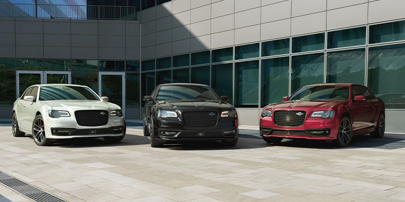 Three Chrysler 300C sedans in white, black, and red parked in front of a modern building