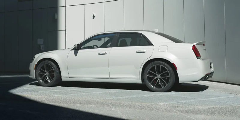 Side view of a white Chrysler 300 sedan with dark wheels, parked against a white building