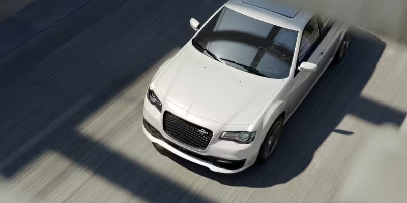 Overhead view of a white Chrysler 300 sedan driving on a highway, casting strong shadows on the road