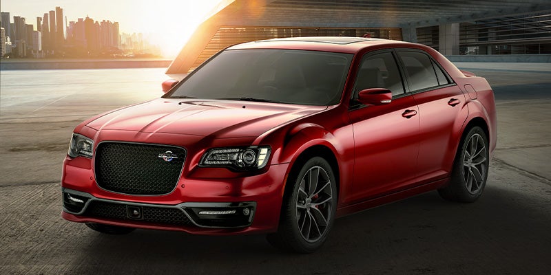 A glossy red Chrysler 300C parked on a concrete lot with a city skyline in the background