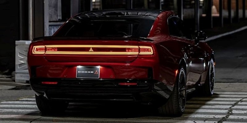 Rear view of a dark red Dodge Challenger parked on a street at night, with illuminated taillights