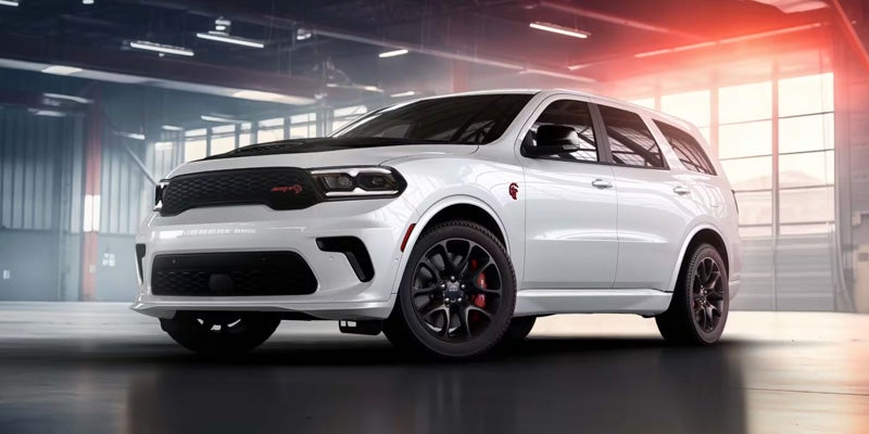 Side-by-side comparison of two SUVs: a white Dodge Durango parked inside a modern showroom and a blue Volkswagen SUV driving on a winding road