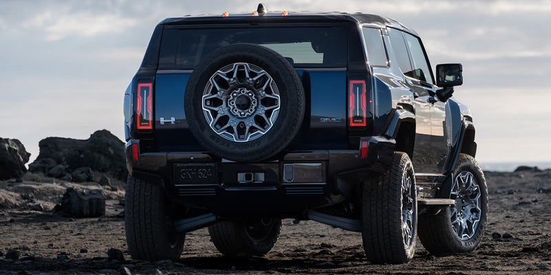 Rear view of a black electric Hummer EV parked on a rocky, dark landscape under a cloudy sky