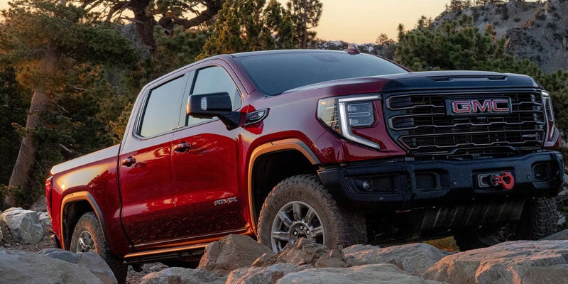 Red GMC Sierra AT4X AEV Edition pickup truck traversing a rocky off-road terrain