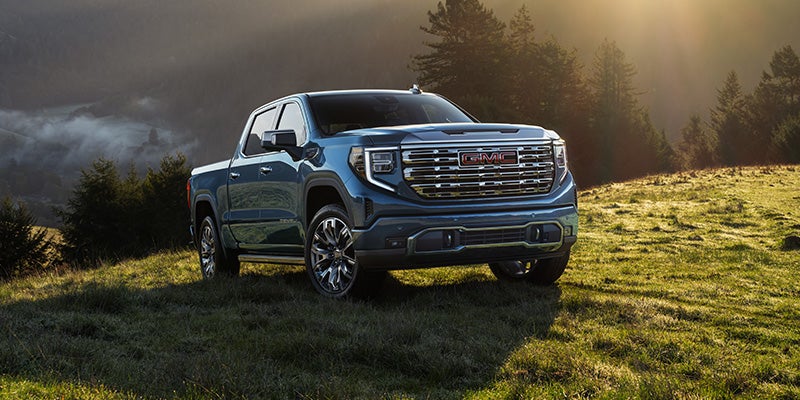 A dark blue GMC Sierra pickup truck parked on a grassy hillside with misty mountains and trees in the background
